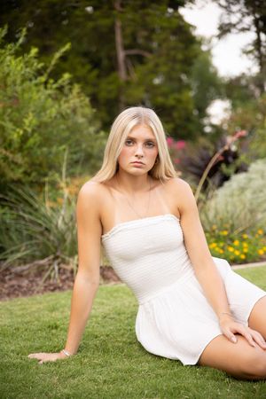 A flowing white summer dress is featured against a lush garden backdrop with green grass and flowers.