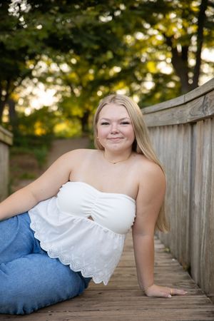 A person in a white dress and blue jeans reclines on a wooden boardwalk during a golden hour photoshoot.