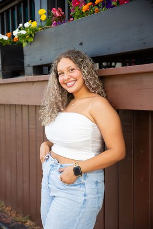 Colorful flowers decorate a wooden fence behind someone wearing a white top and light denim jeans.