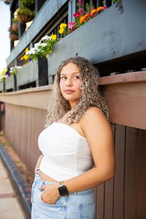 A series of outdoor portrait photos showing someone in a white top and denim against a brown wall with colorful flowers above.