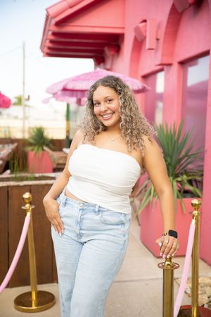 Four connected photos showing someone wearing a white top and light blue jeans posing against a pink building exterior.