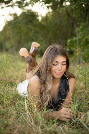 A person in a dark top lies in tall grass at sunset during an outdoor portrait session.
