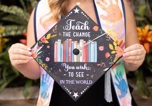 Graduation cap decorated with colorful flowers and inspirational text on black background displayed in outdoor setting.