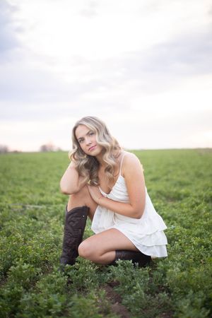 A person in a white dress sits gracefully in a lush green field during golden hour.