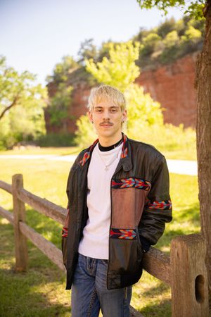 Casual portrait outdoors featuring southwestern style jacket with decorative pattern against autumn foliage and wooden fence.