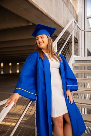Graduate in bright blue cap and gown poses on concrete steps during graduation photoshoot.