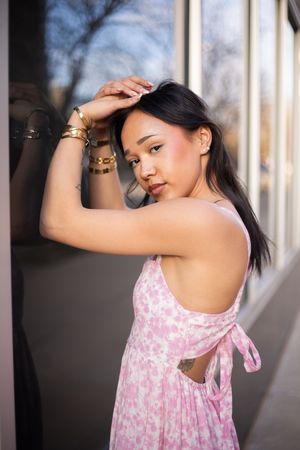 Woman in pink floral sundress poses gracefully against a sunlit outdoor corridor with columns.