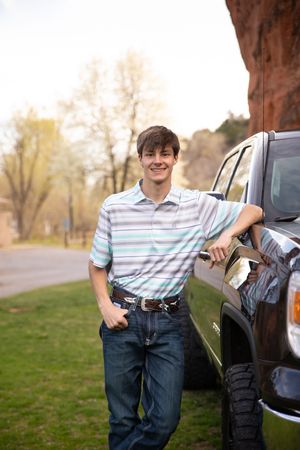 Casual portrait of someone in a striped polo shirt leaning against a black pickup truck on a spring day.