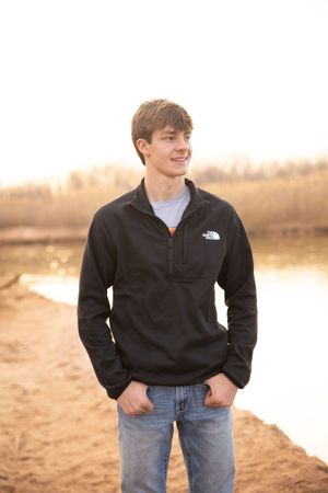 Person wearing a black North Face fleece and jeans poses outdoors at sunset by a lake.