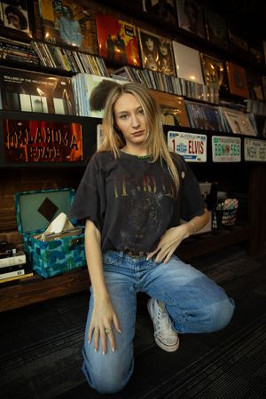 A casual scene at a record store with vinyl albums displayed on shelves while someone poses in jeans and a t-shirt.