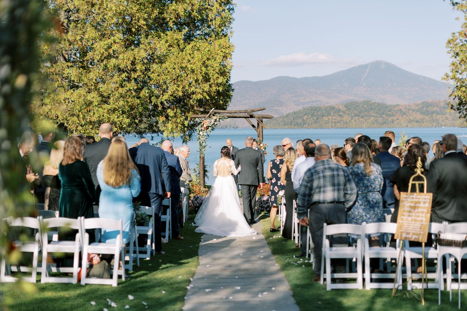 A joyful outdoor wedding ceremony with guests seated in rows and a couple exchanging vows under natural lighting.