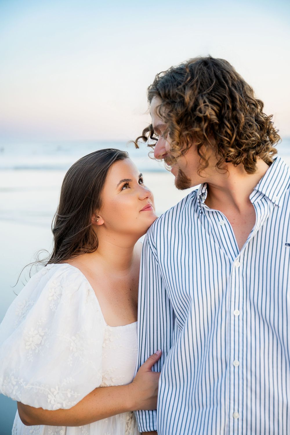 A couple shares tender moments against a soft beach backdrop during sunset.