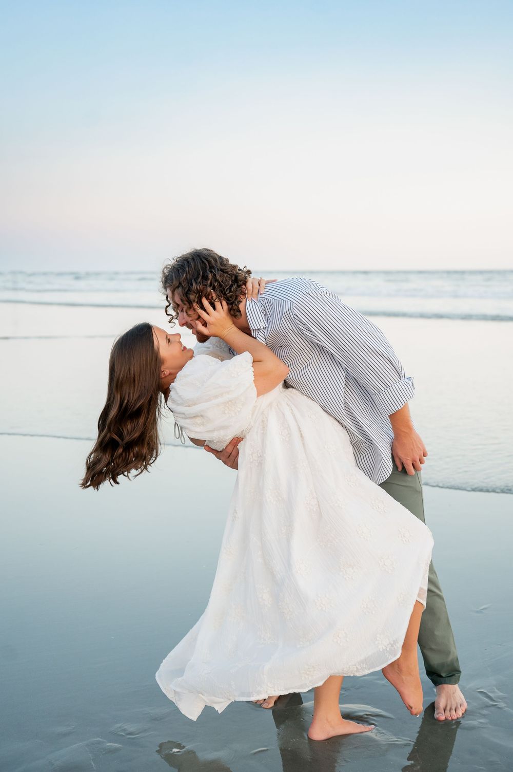 A romantic couple dips and dances together on a serene beach at sunset.