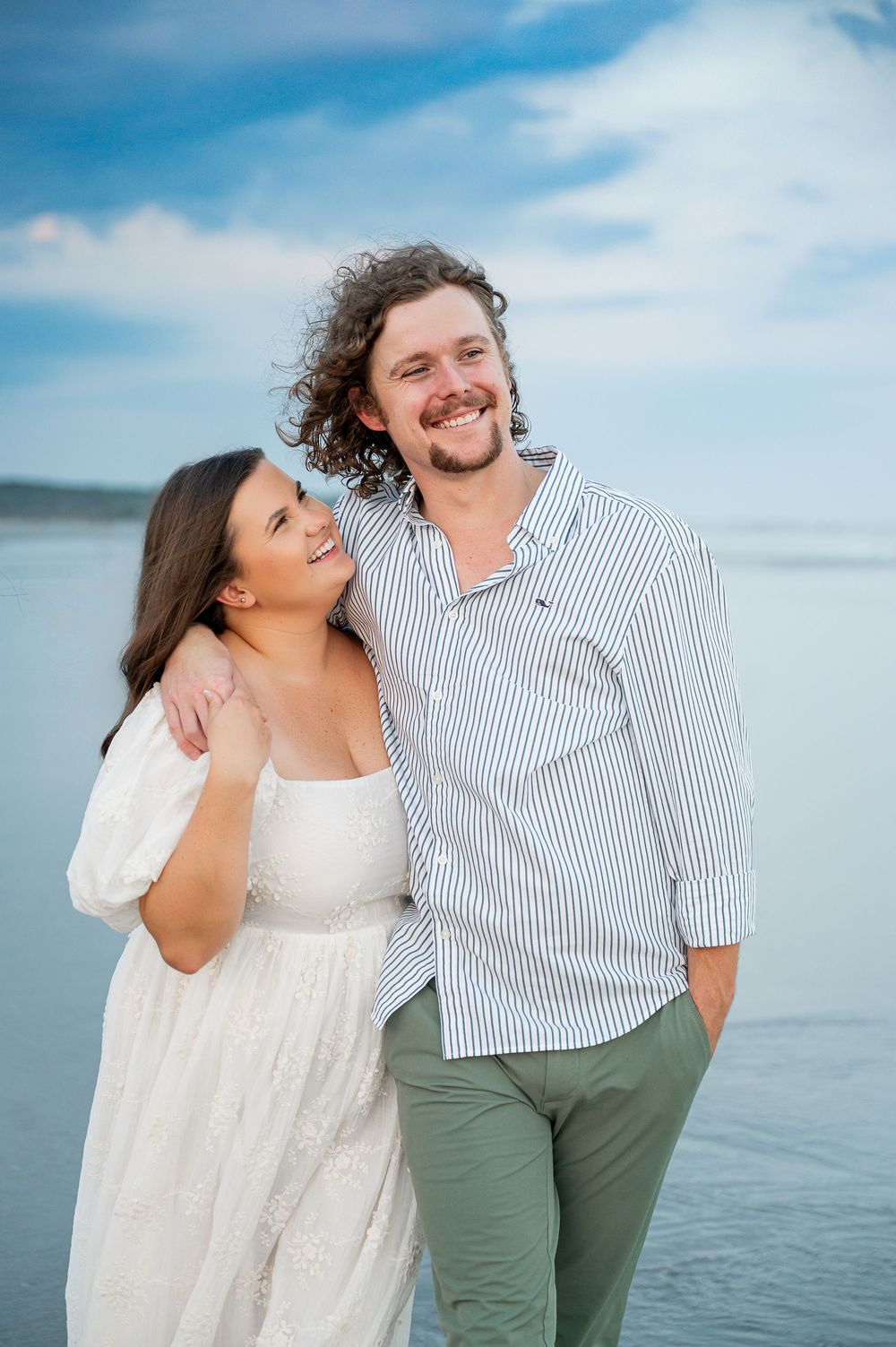 A couple laughs together while posing for photos on a cloudy beach day.