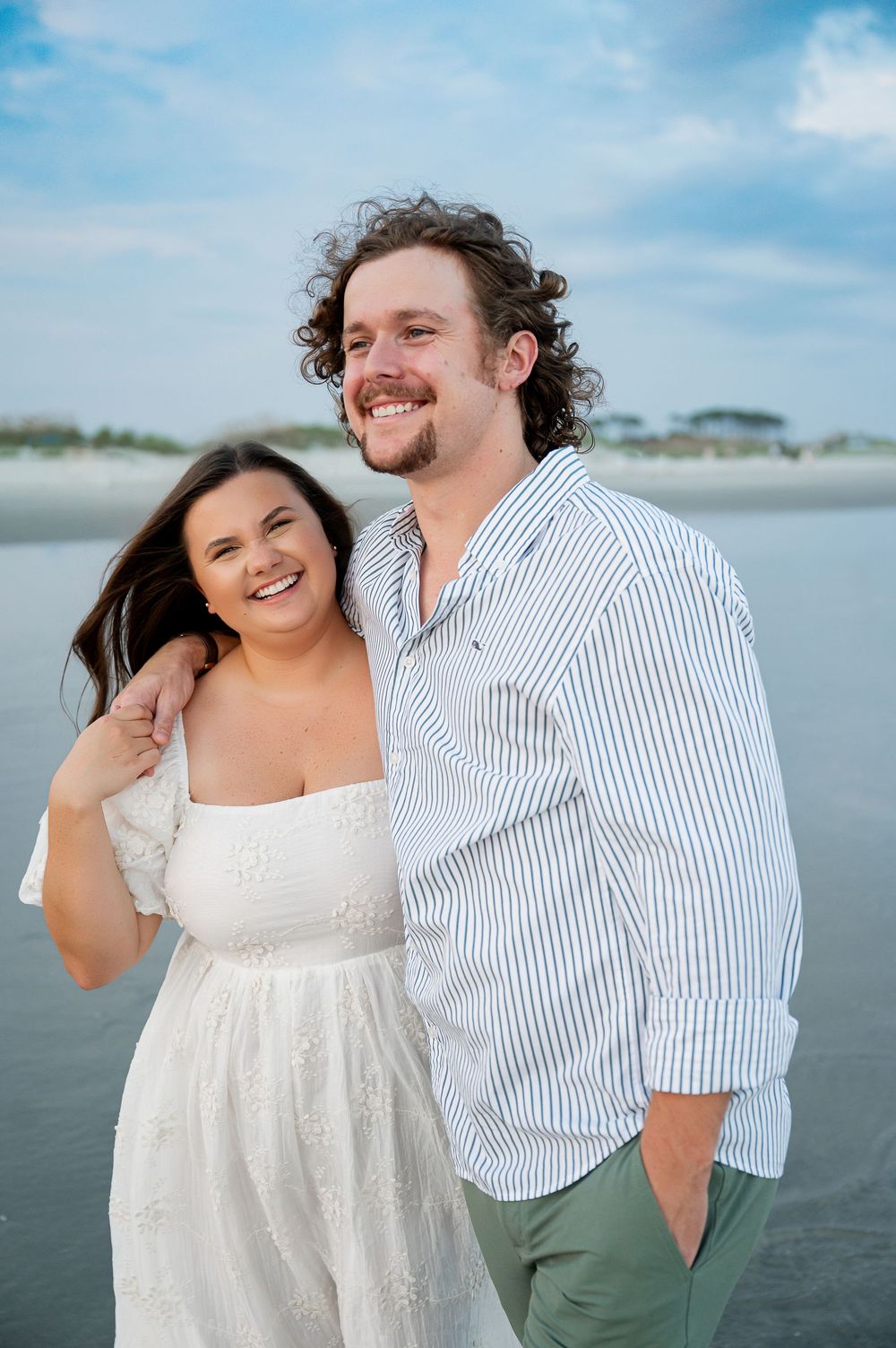 A couple shares joyful laughter during their beach photoshoot on a bright summer day.