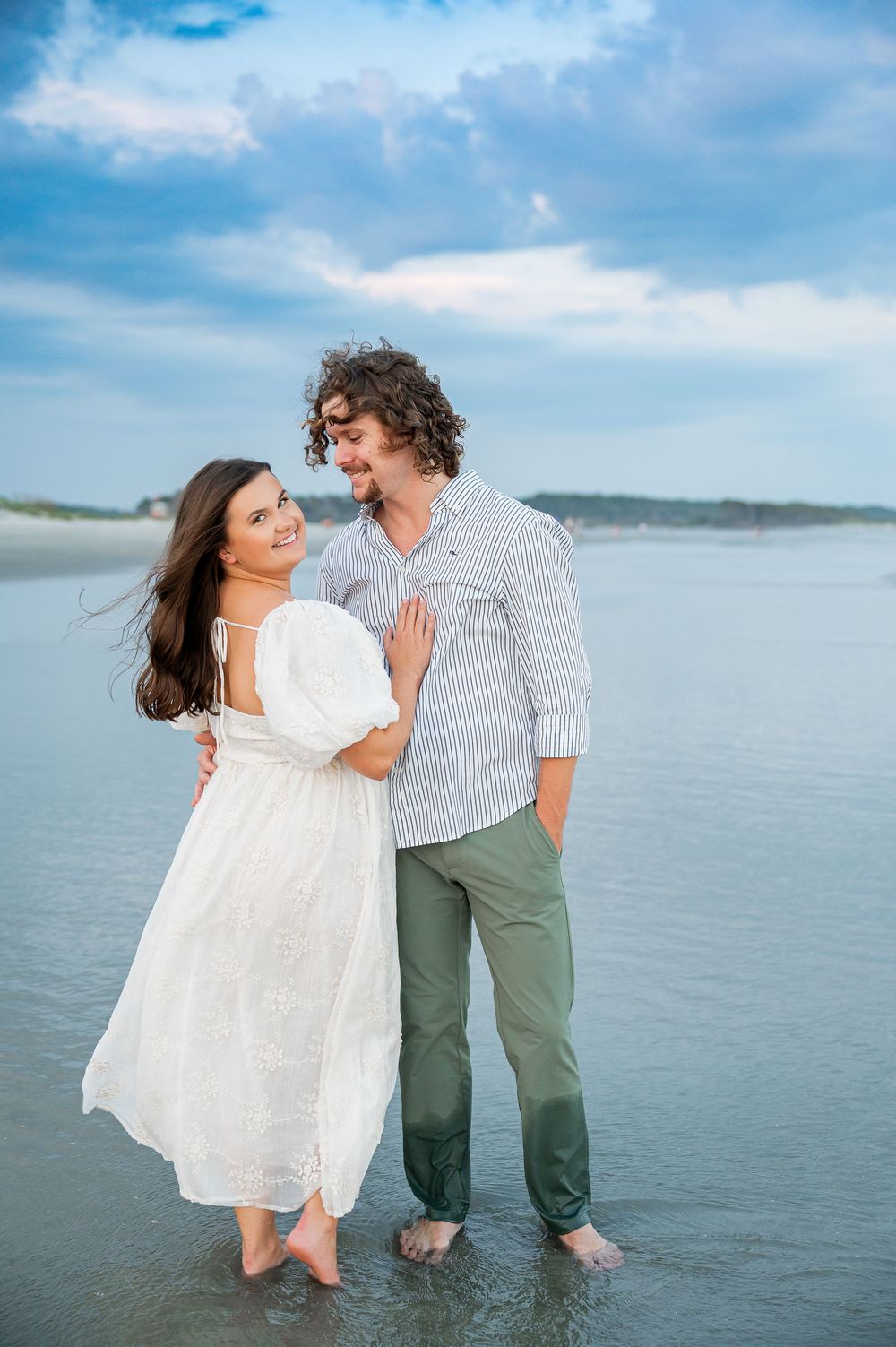 A couple wades through calm ocean waters during a romantic beach photoshoot.