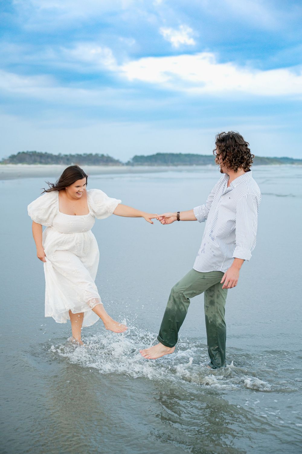 A couple splashes and plays in shallow ocean water during their beach photo session.