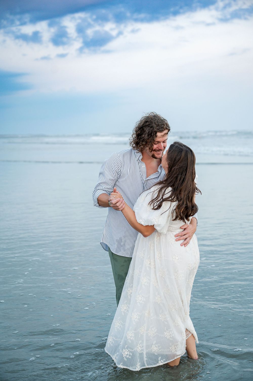 A couple dances and embraces in the shallow ocean water during sunset.