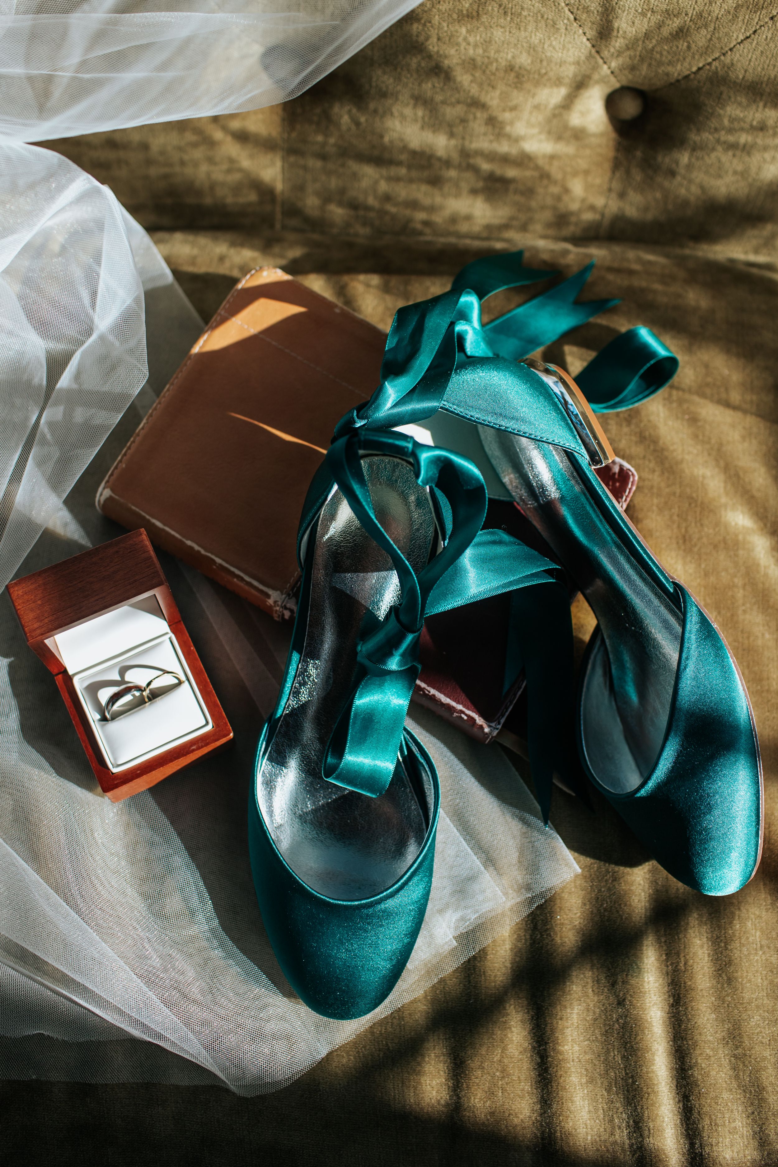 Elegant teal velvet wedding shoes with straps arranged artistically on a textured surface with soft lighting.
