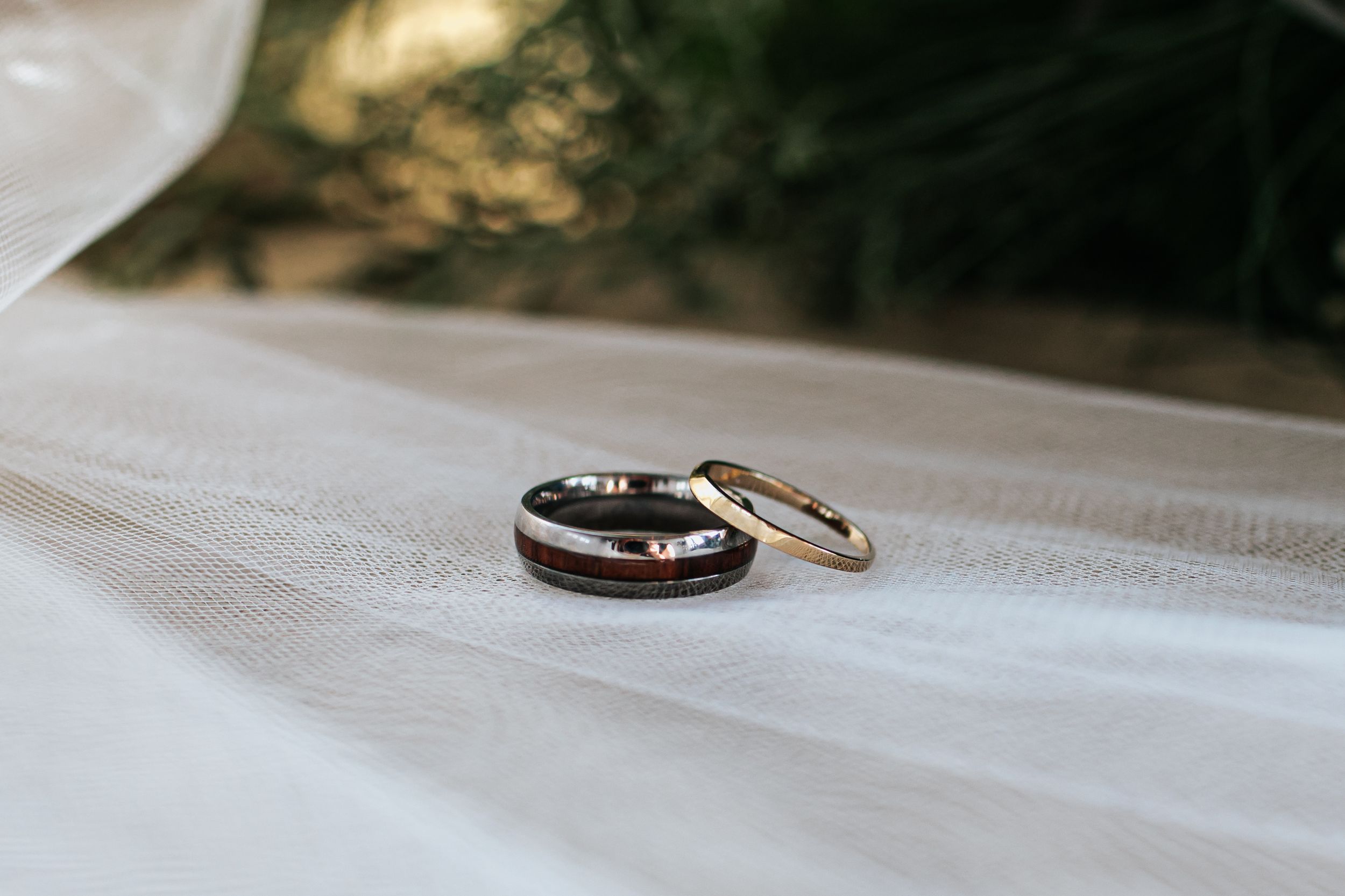 Two wedding rings sit side by side on a white textured surface in soft natural lighting.