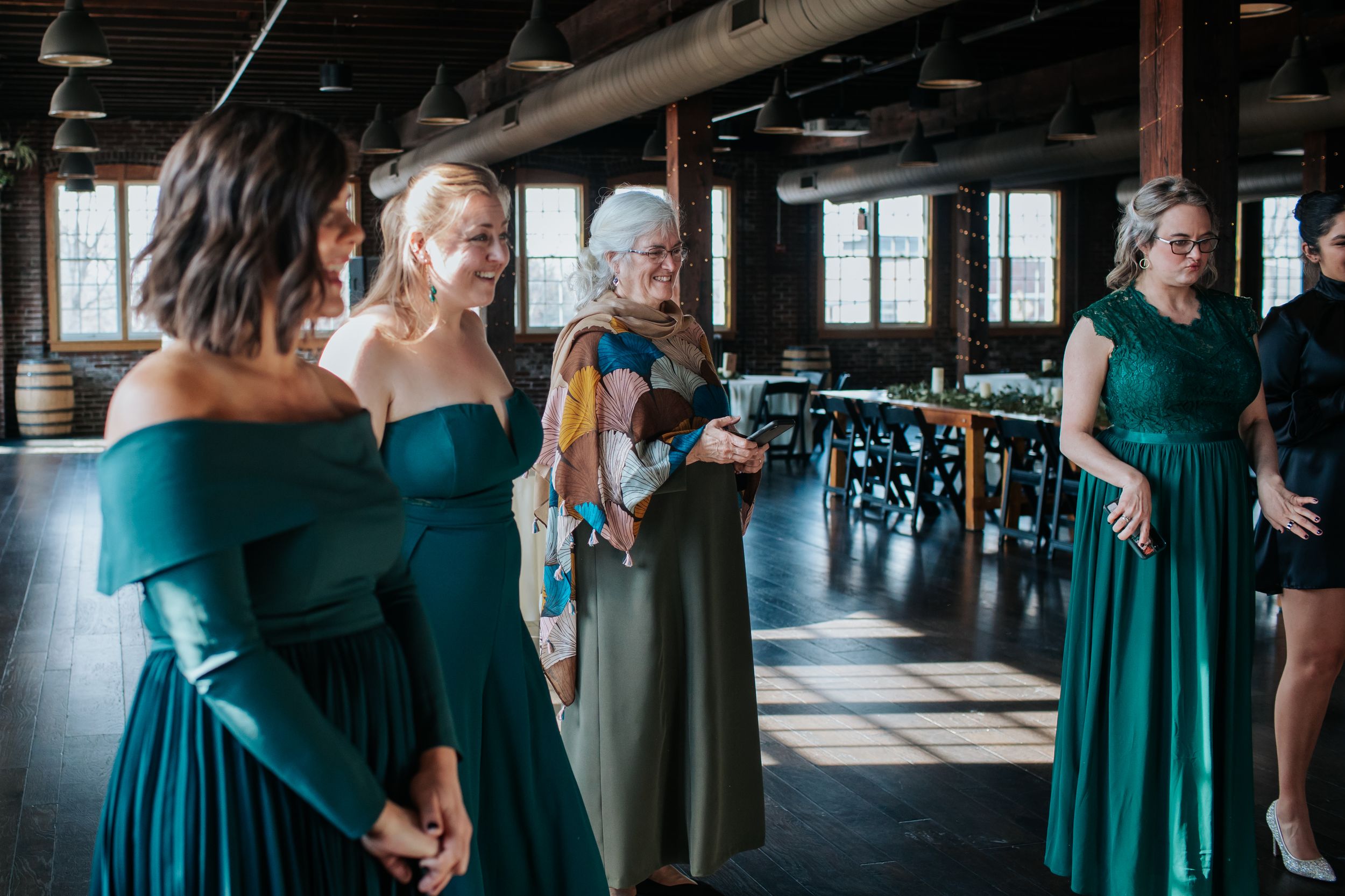 A group of people in teal dresses gather in a rustic wooden interior venue for a formal event.