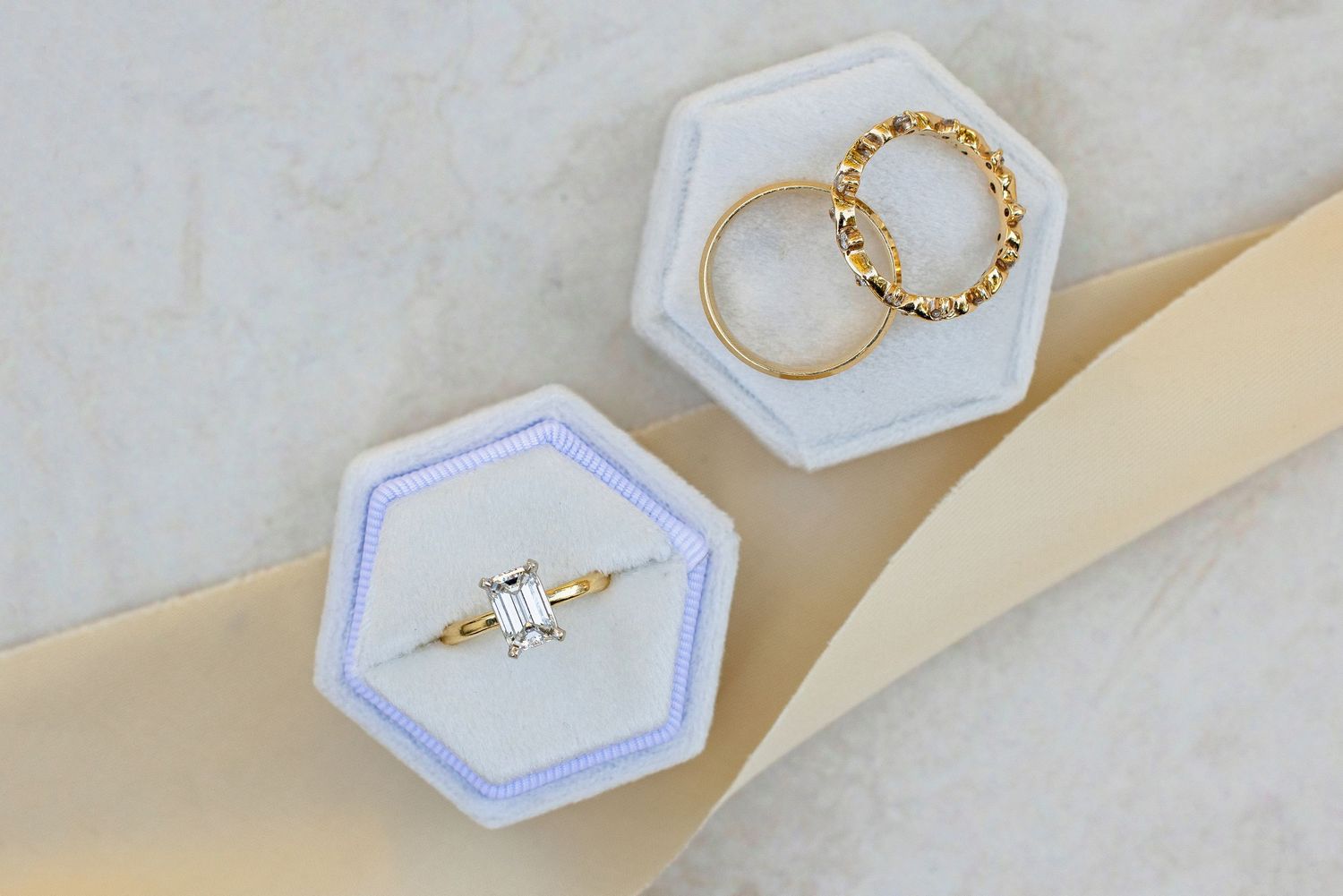 Gold twisted chain bracelet and delicate ring displayed in hexagonal white jewelry boxes on marble surface.