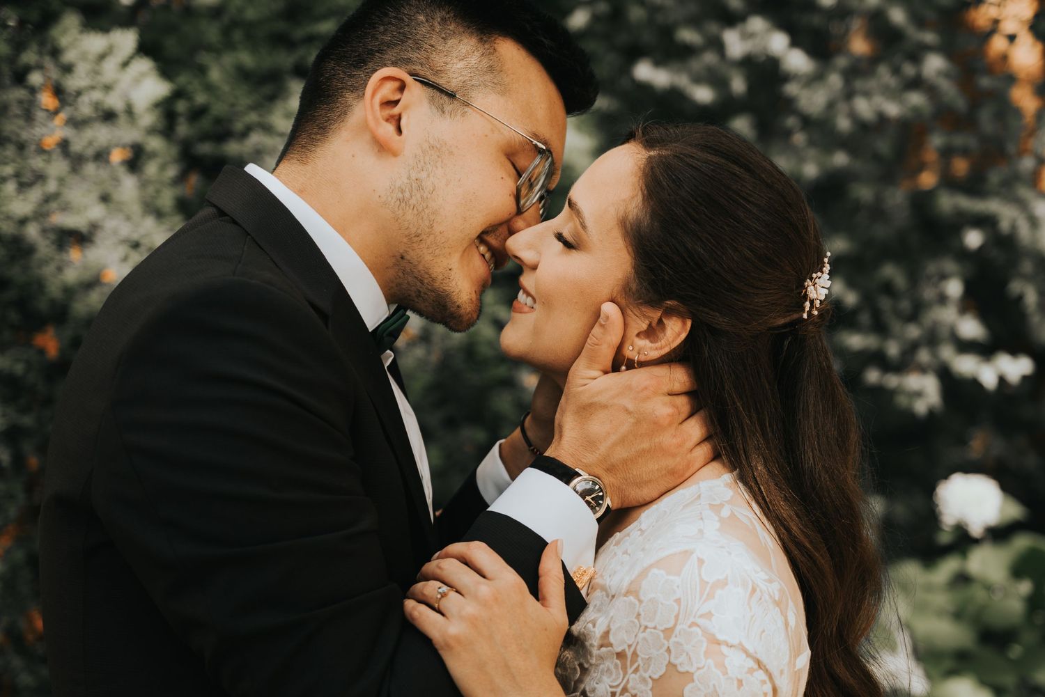 Romantic wedding couple embraces and kisses in a lush outdoor garden setting with soft natural lighting.