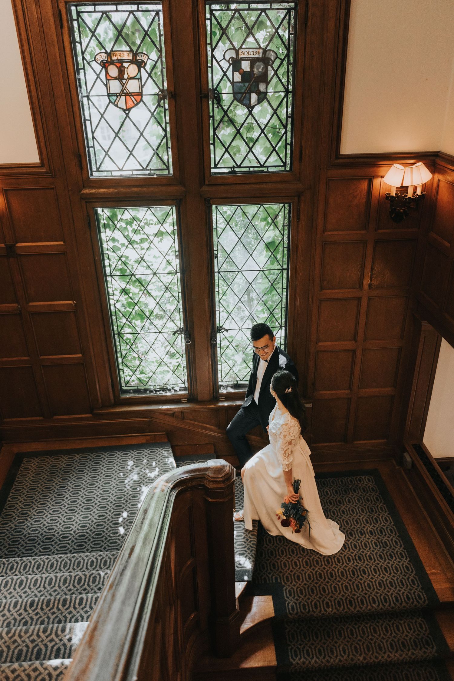 A sequence of candid moments on an elegant staircase with wood paneling and stained glass windows.
