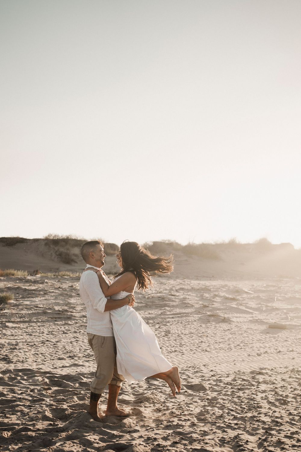Wide-angle cinematic shot of a couple surrounded by wild beach grass and sandy ridges.