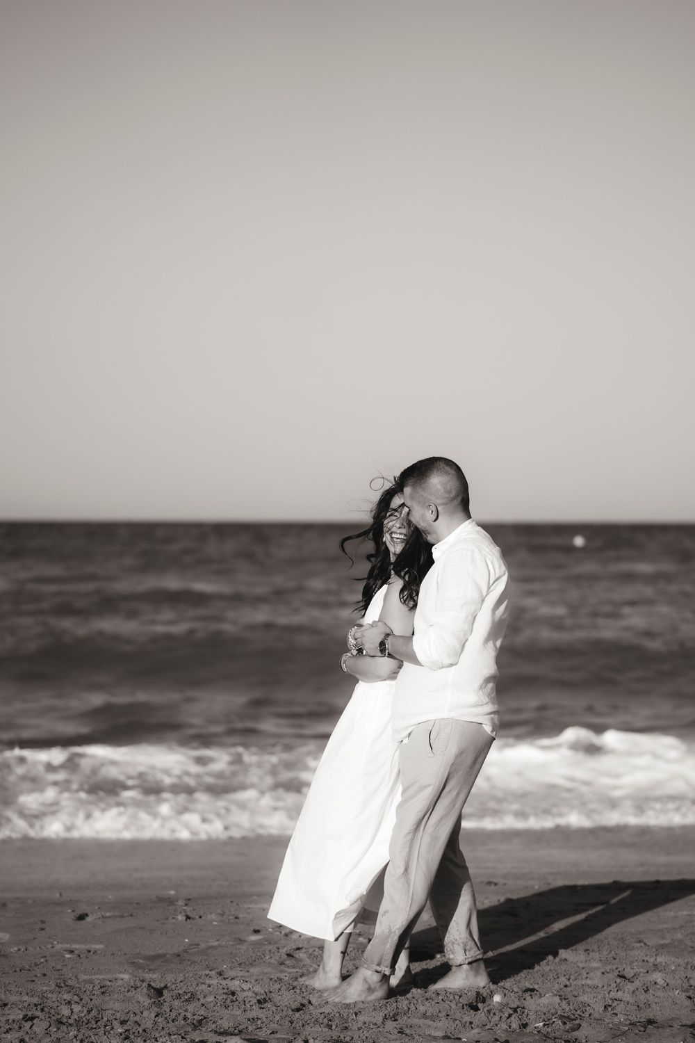 Black and white emotional portrait of a couple holding each other on a vast sandy beach.