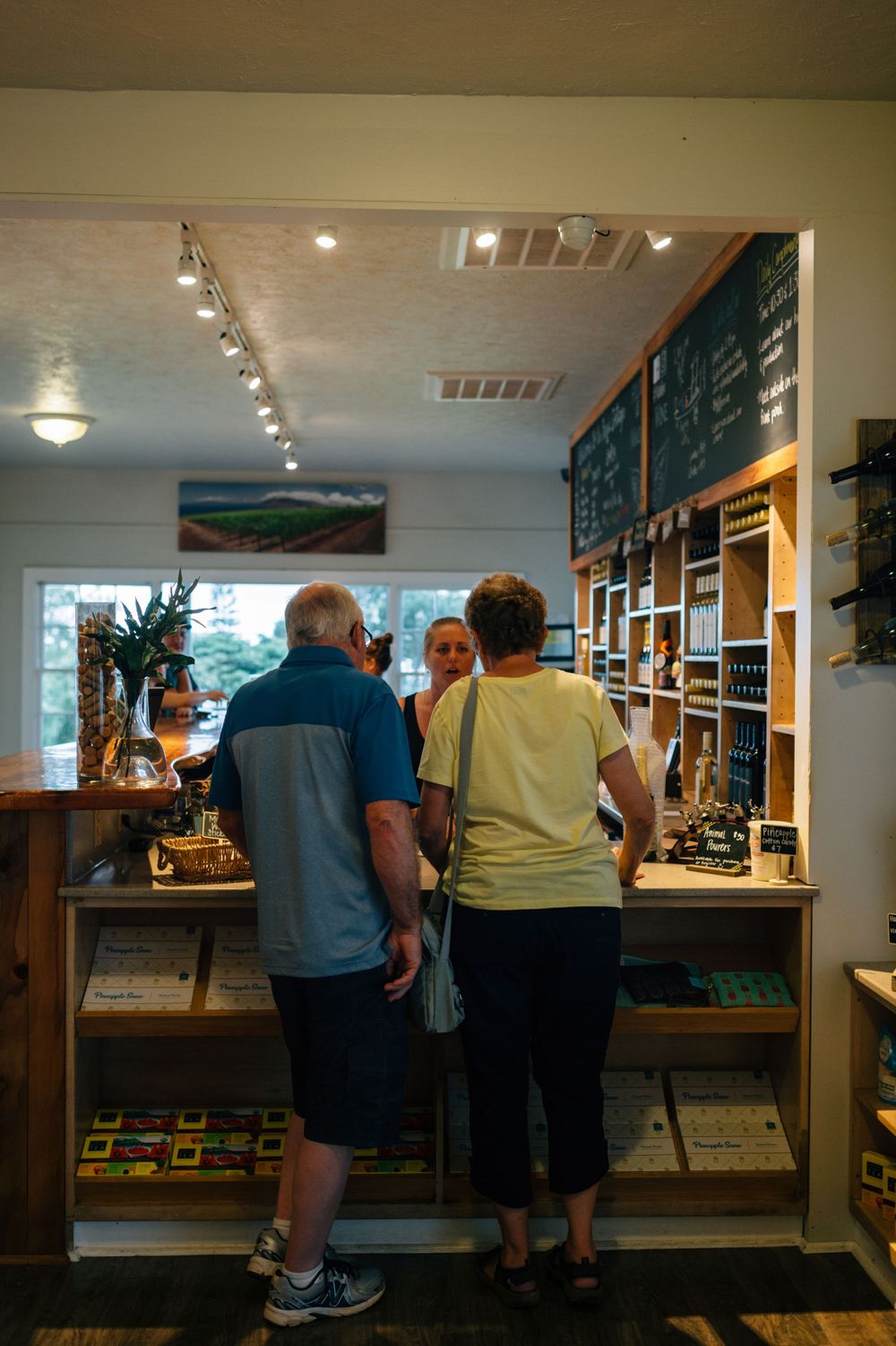 Customers seated at a rustic bar counter with wooden shelving and wine bottles displayed on the back wall.