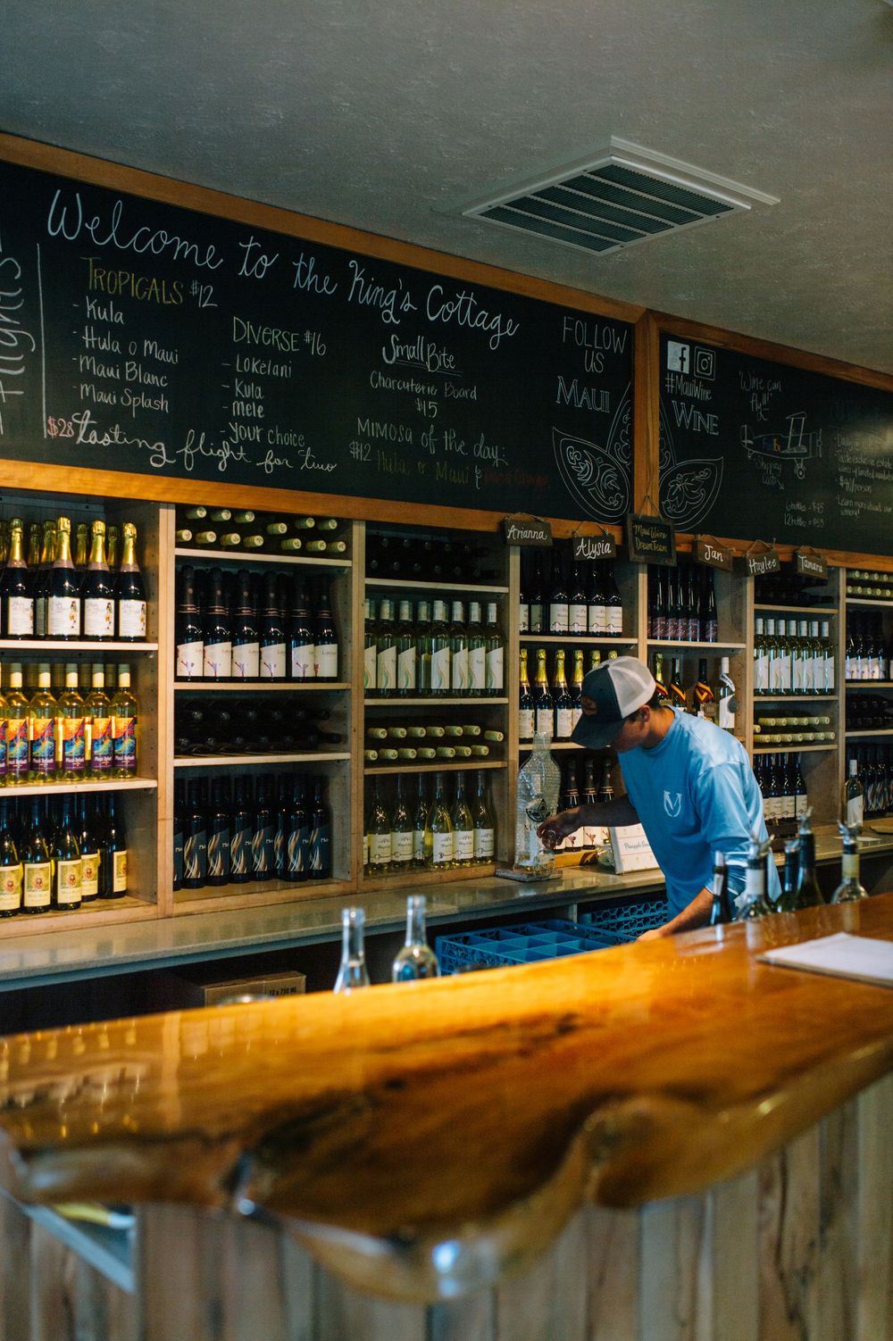 Long wooden bar counter with wine bottles and chalkboard menus displayed on shelves.