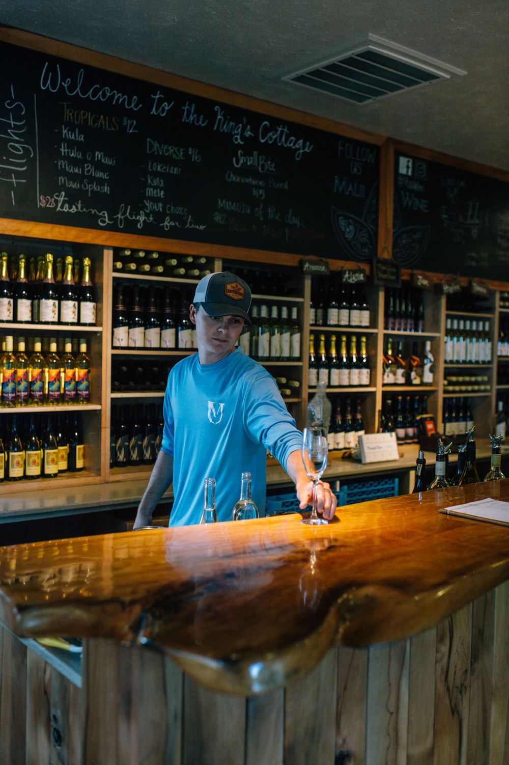 Bartender pouring drinks behind a polished wooden bar with extensive wine bottle display.