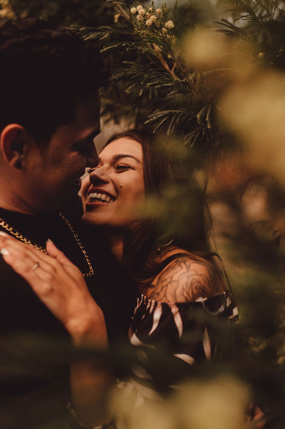Romantic couple shares tender moments through foliage in warm evening light.