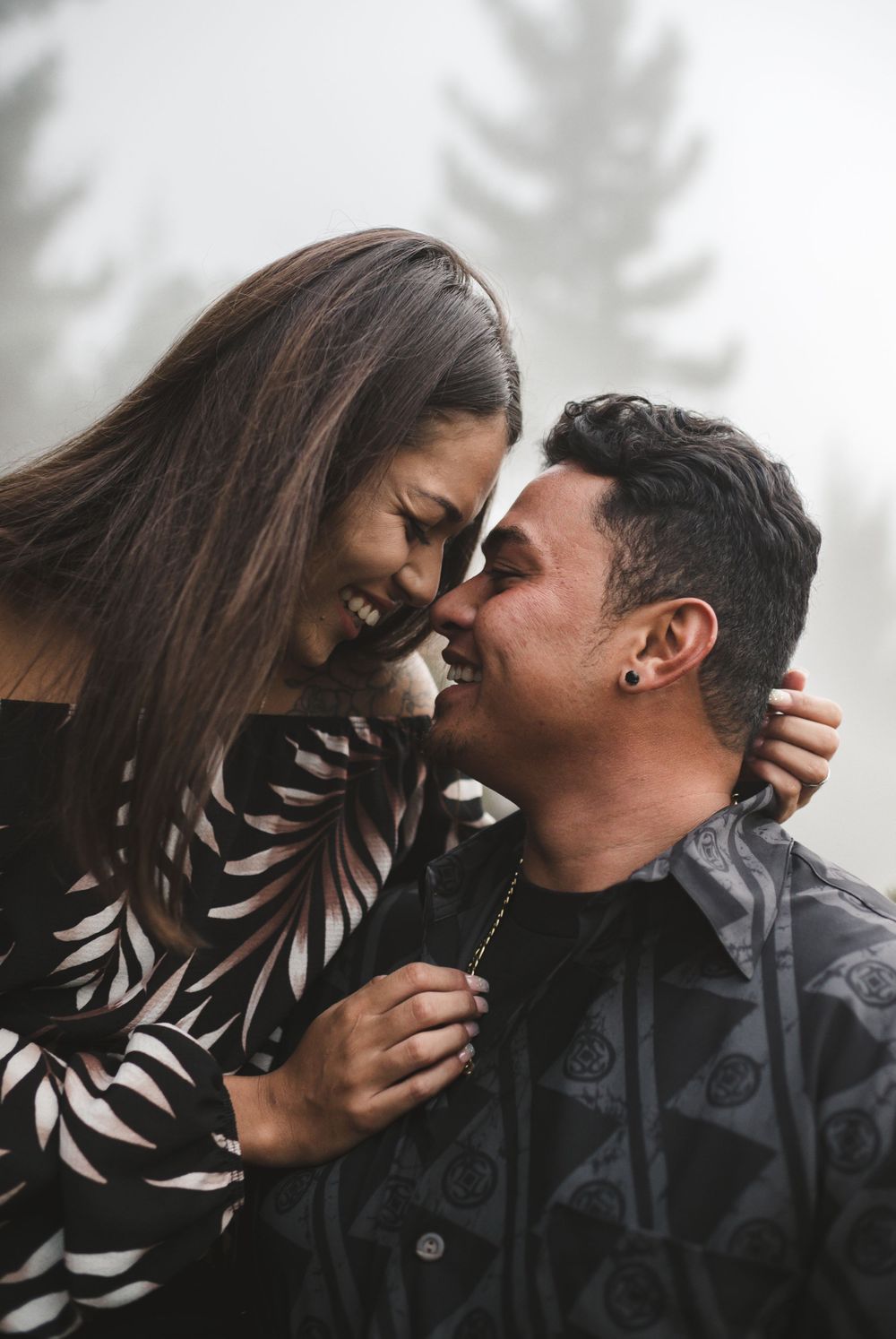 Couple shares intimate moments against a misty forest backdrop.