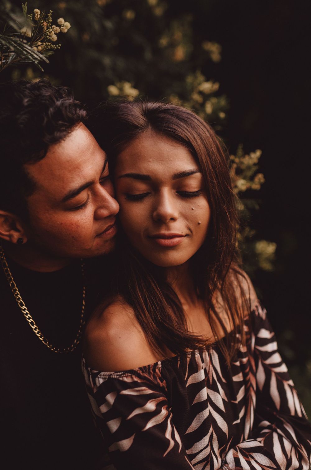 Romantic couple shares tender moments in moody lighting with natural foliage.