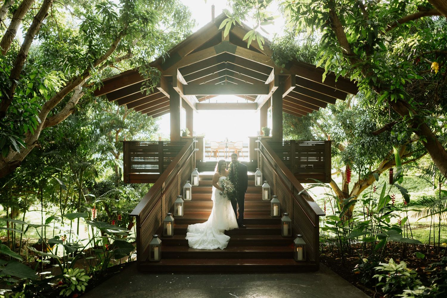Sunlight streams through trees at an outdoor wedding venue with wooden architectural details.