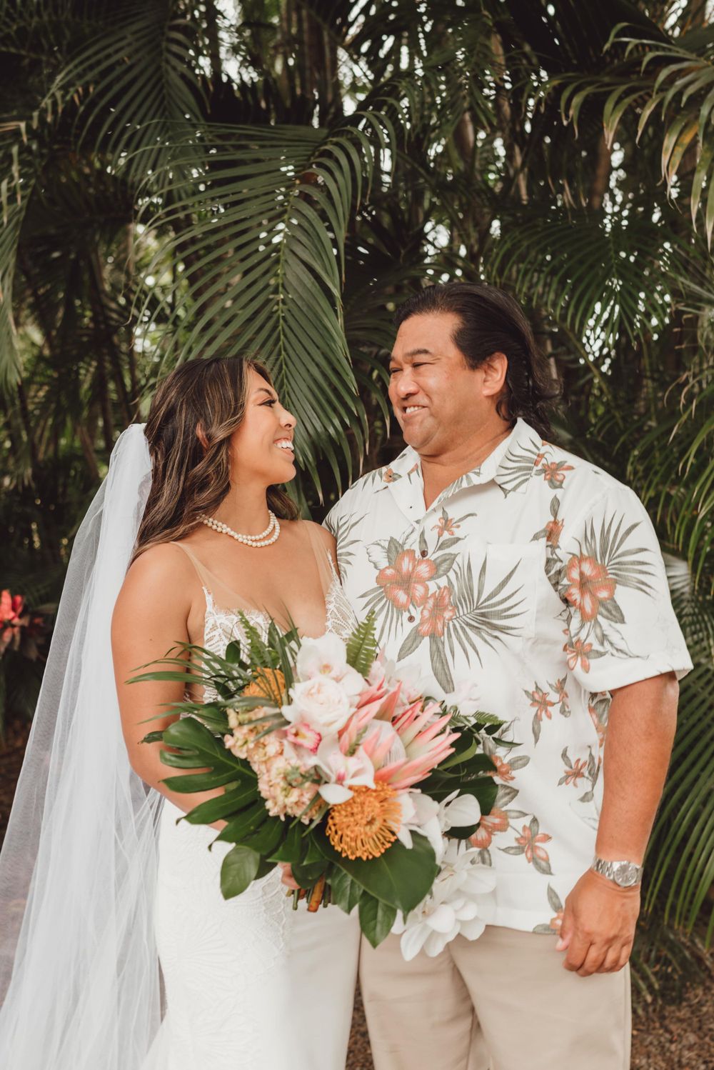 A couple shares an intimate moment surrounded by tropical palm fronds at their outdoor wedding ceremony.
