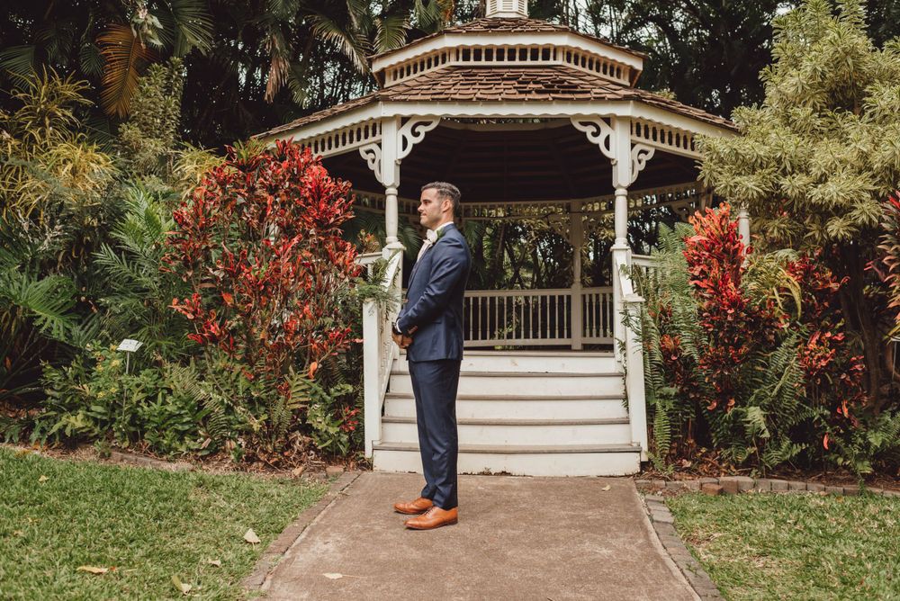 A romantic first look moment between newlyweds at a white garden gazebo surrounded by lush tropical landscaping.