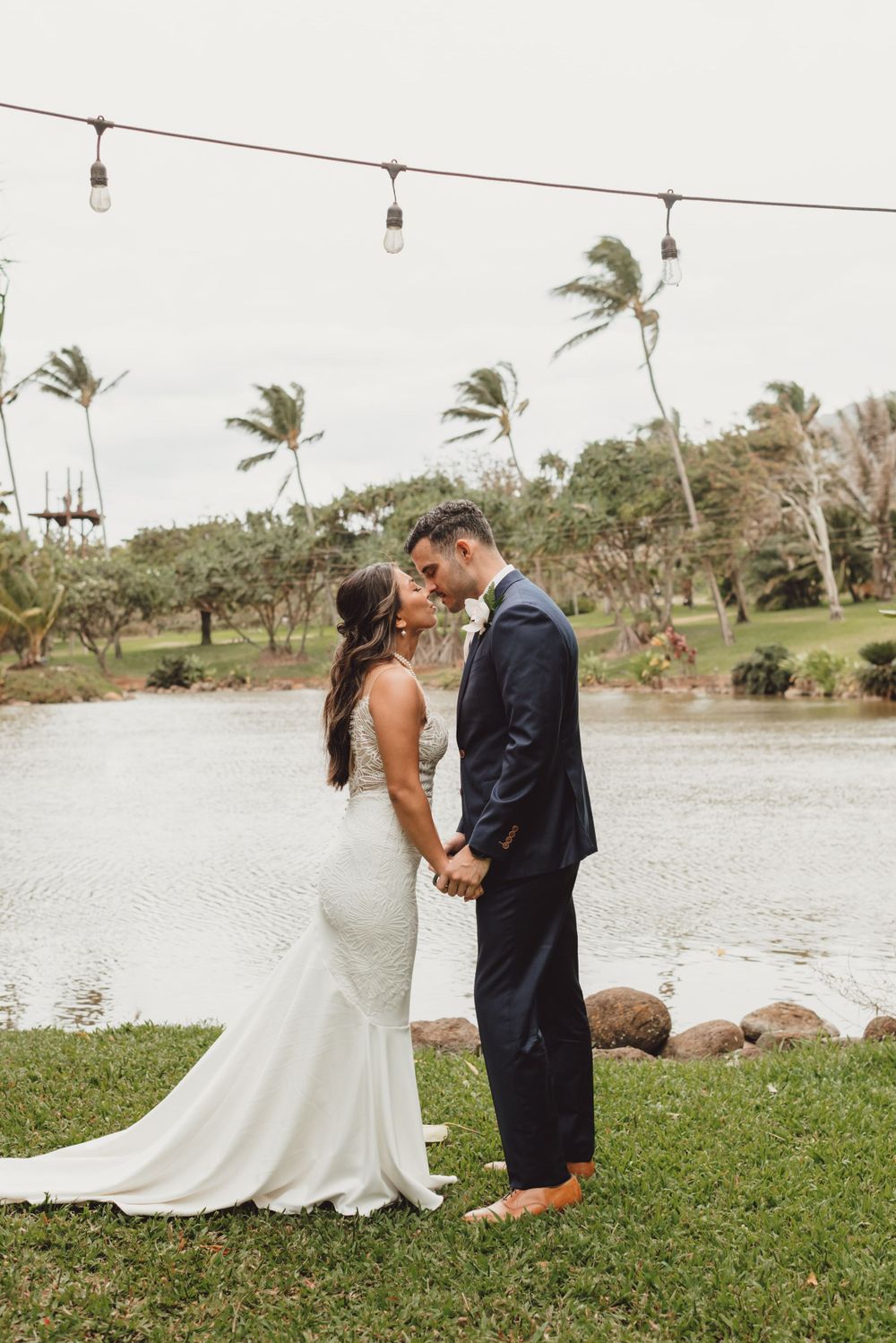 Wedding couple shares intimate first look moment by a waterfront with palm trees swaying in the background.