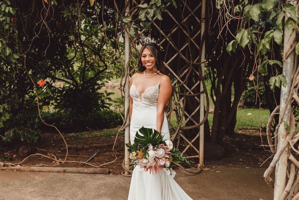 Elegant wedding scene with white lattice archway decorated with climbing vines and tropical greenery.