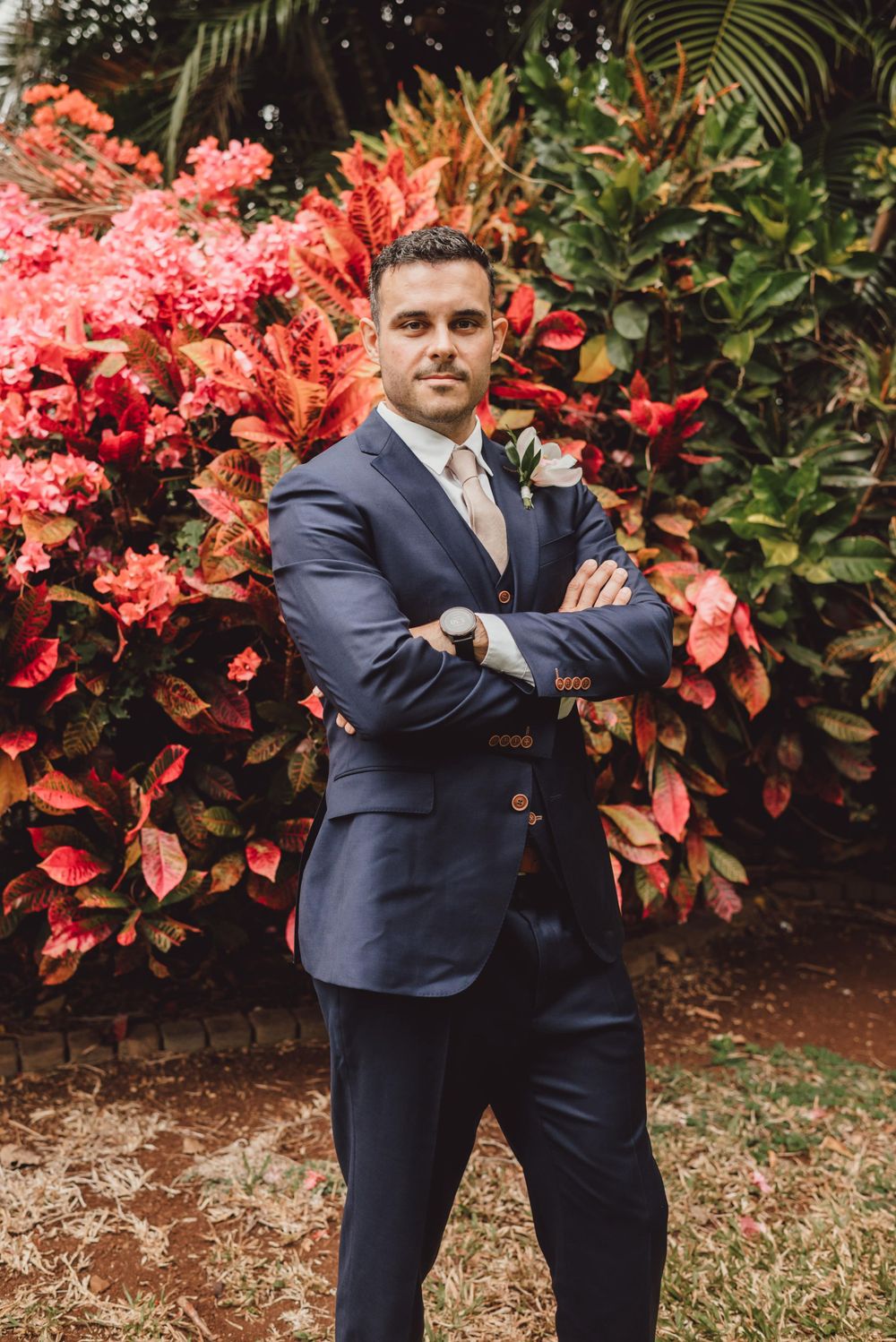 Navy suited figure poses playfully against a backdrop of bright coral-colored tropical plants.