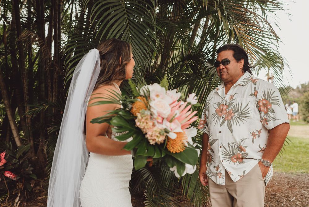 A couple shares an intimate moment surrounded by tropical palm fronds at their outdoor wedding ceremony.