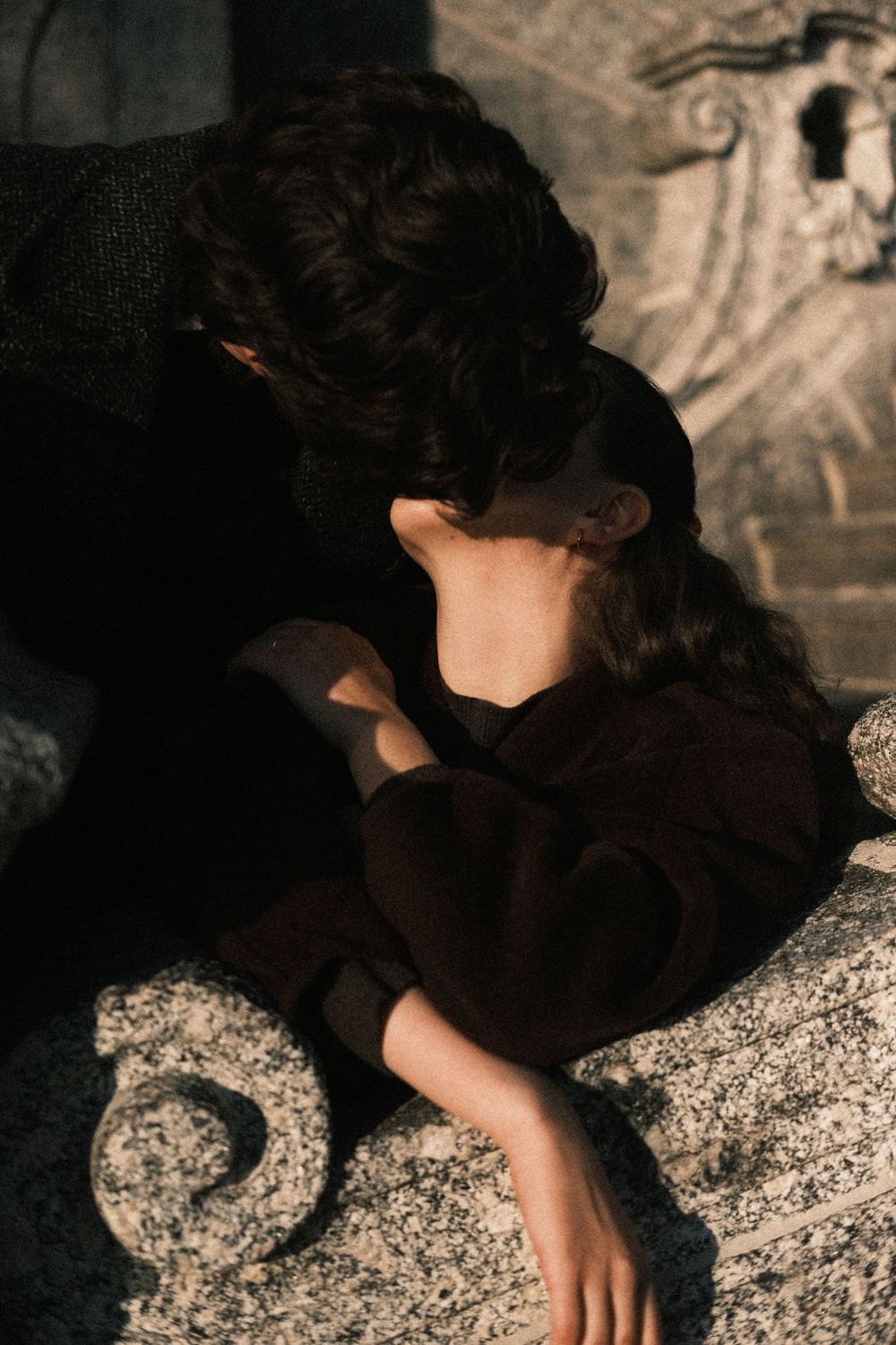 A series of artistic photographs showing a person in black clothing resting against textured stone surfaces.