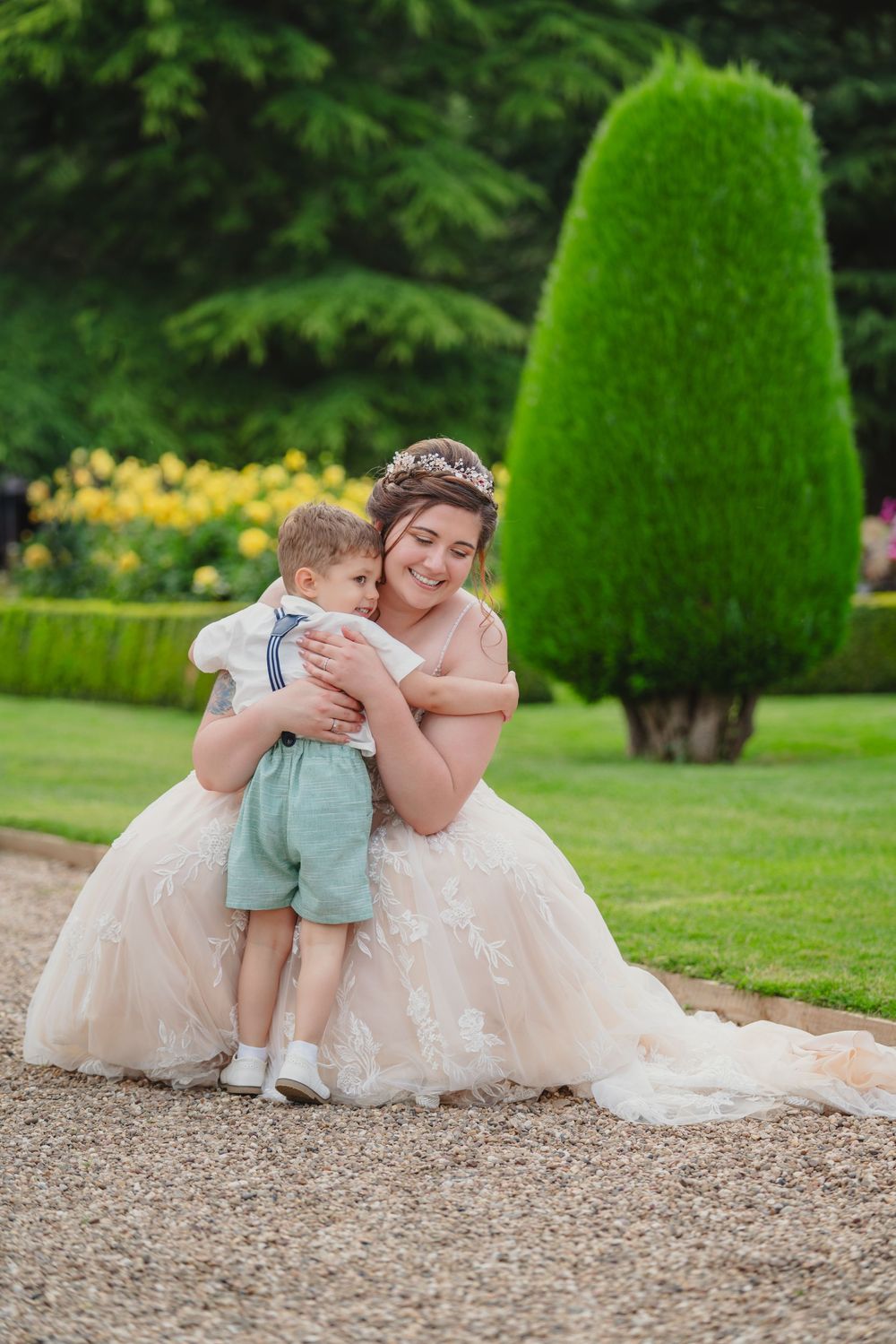 Sweet moment captured on gravel path with bride in lace gown interacting with small child.