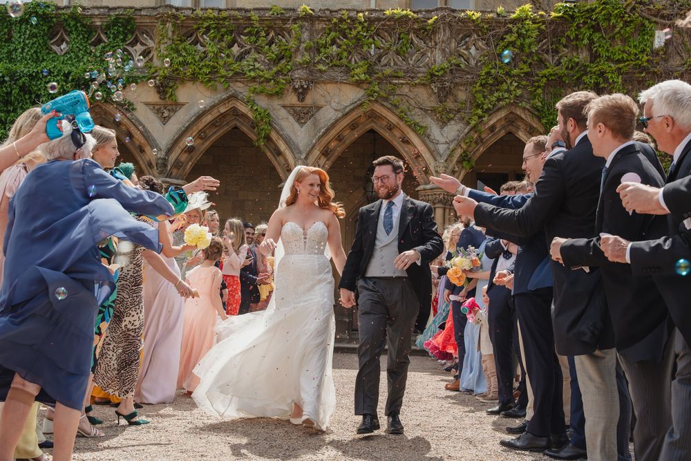 Wedding guests forming an aisle outdoors while throwing flower petals during the celebration.