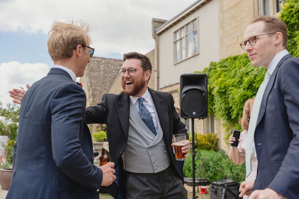Groomsmen in navy suits chat and laugh during outdoor wedding reception.