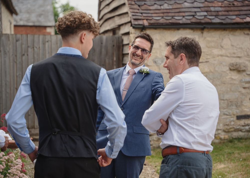 Wedding guests gather outside a rustic barn venue during an outdoor celebration.