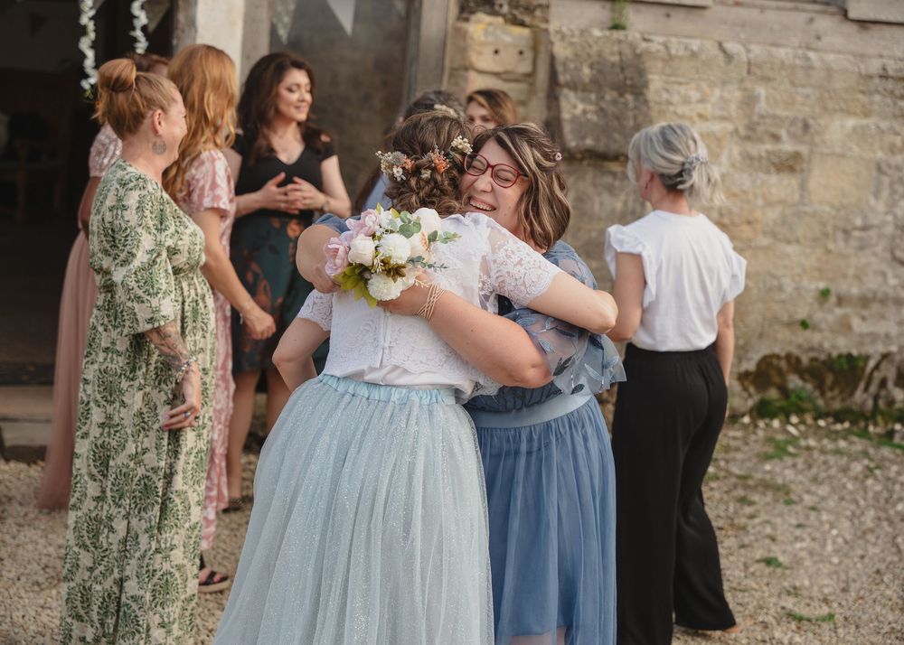 Wedding guests in formal attire gather outside a historic stone building.