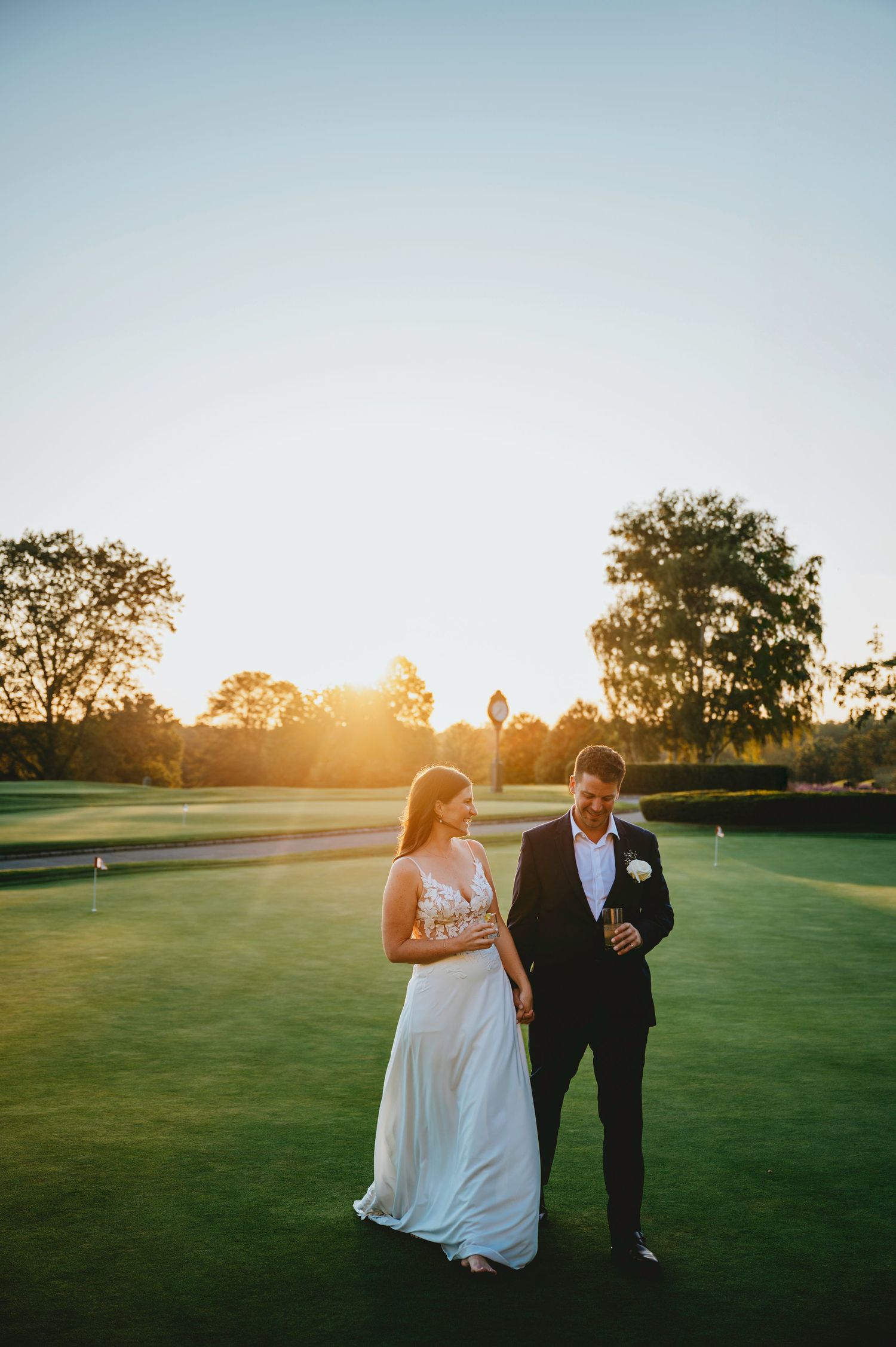 A couple walks together on a lush green golf course at golden hour during sunset.